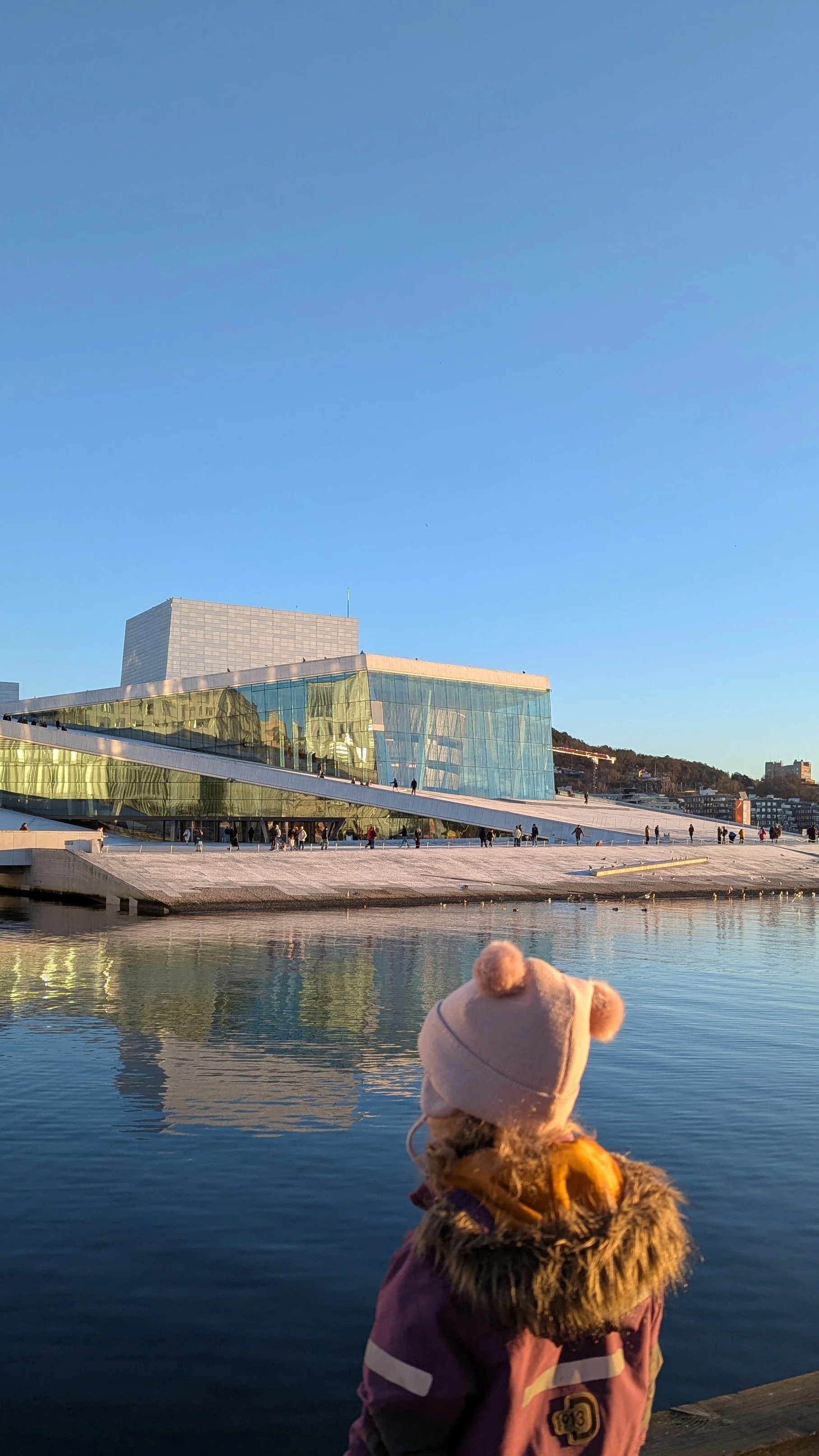 Child in winter clothes looking at the Oslo Opera House